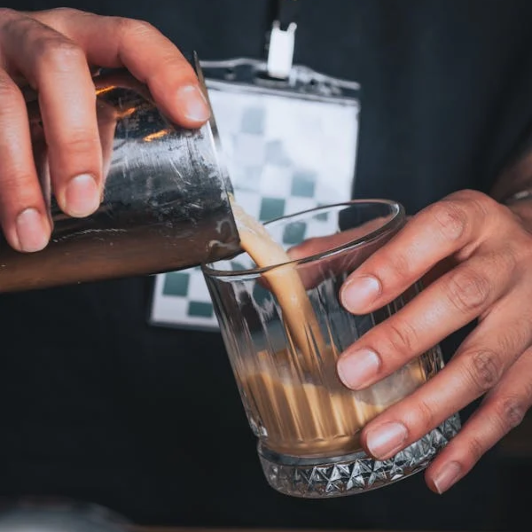 A person pouring a coffee cocktail into a glass made with Cinchona Blend ground coffee