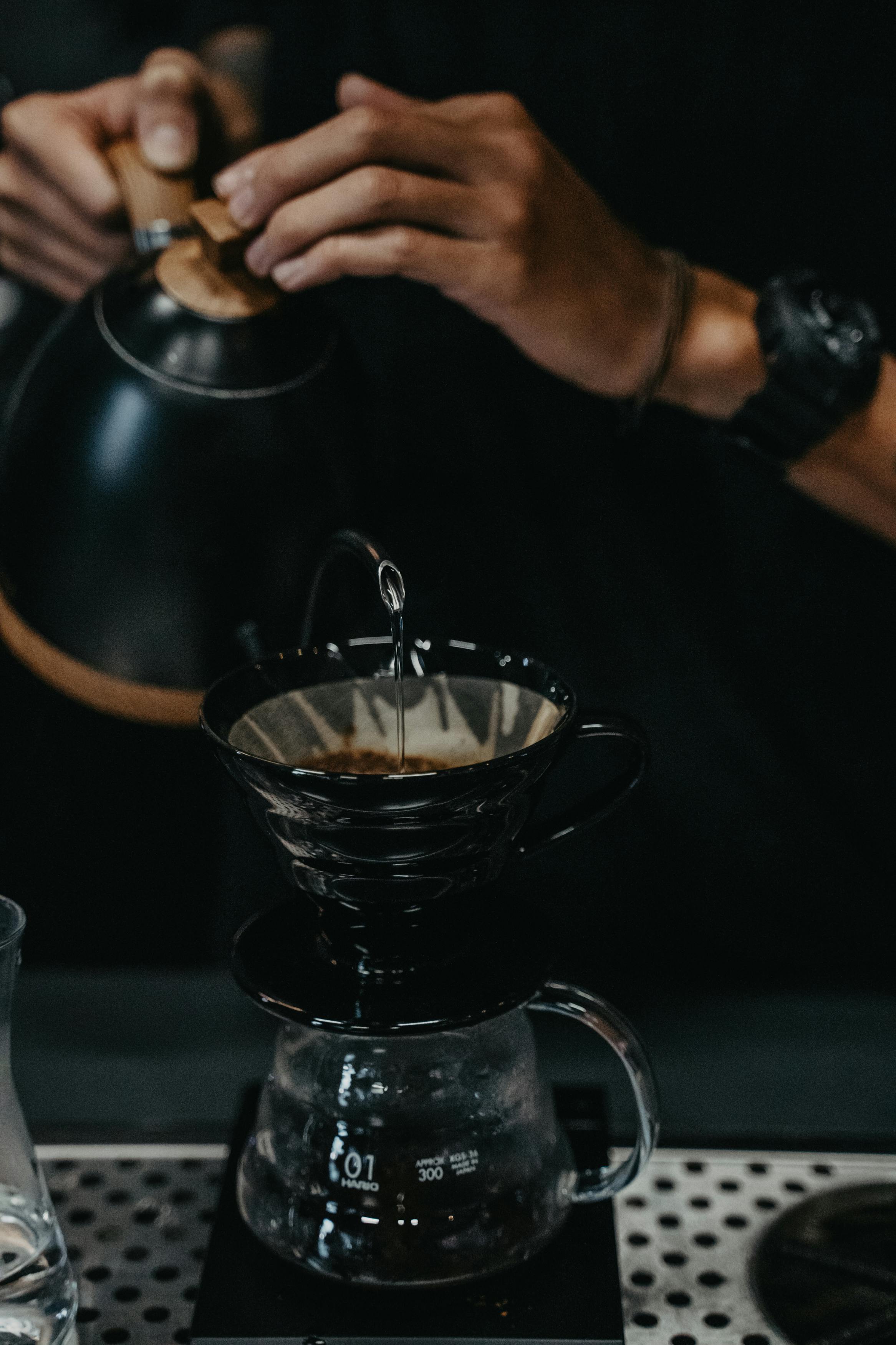 A person brewing Jamaica coffee by slow pouring water over coffee grounds into a Chemex