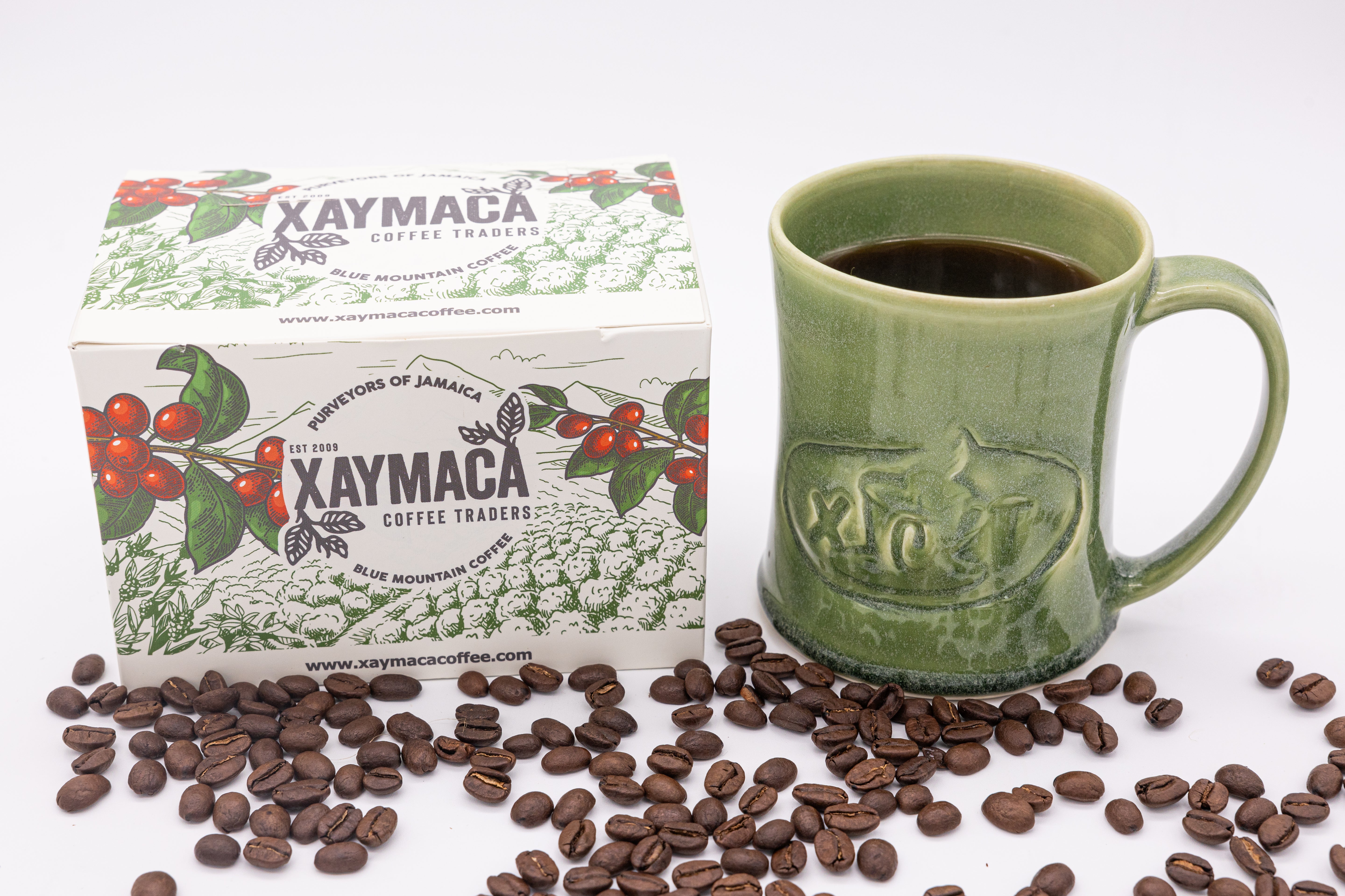 A box of Xaymaca coffee tablets next to a green coffee mug with coffee beans scattered around.