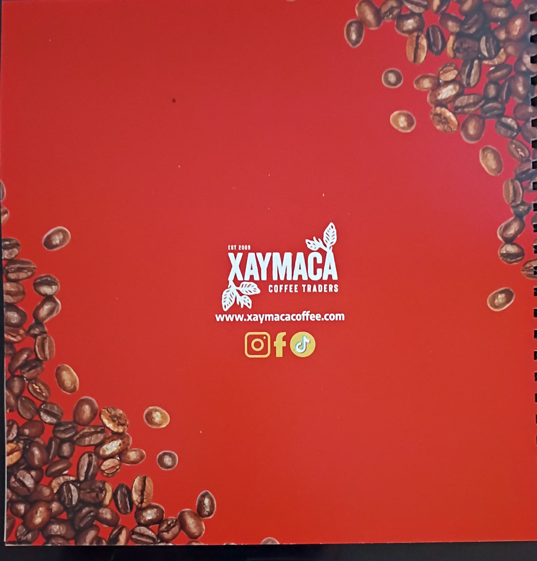 Red notebook with Xaymaca Coffee Traders logo and coffee beans on a dark background