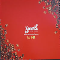 Red notebook with Xaymaca Coffee Traders logo and coffee beans on a dark background
